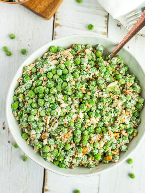 a white bowl with green pea salad and a bronze spoon