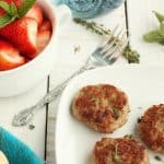Three sausage patties on a plate with strawberries and herbs in the background