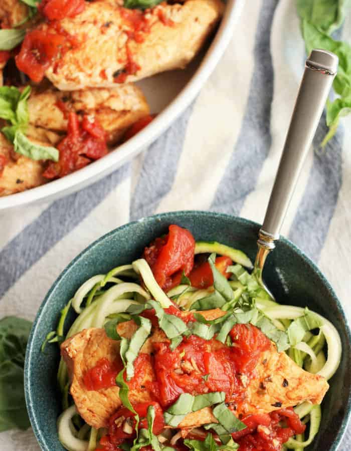 bruschetta chicken on zucchini noodles in a blue bowl with a fork