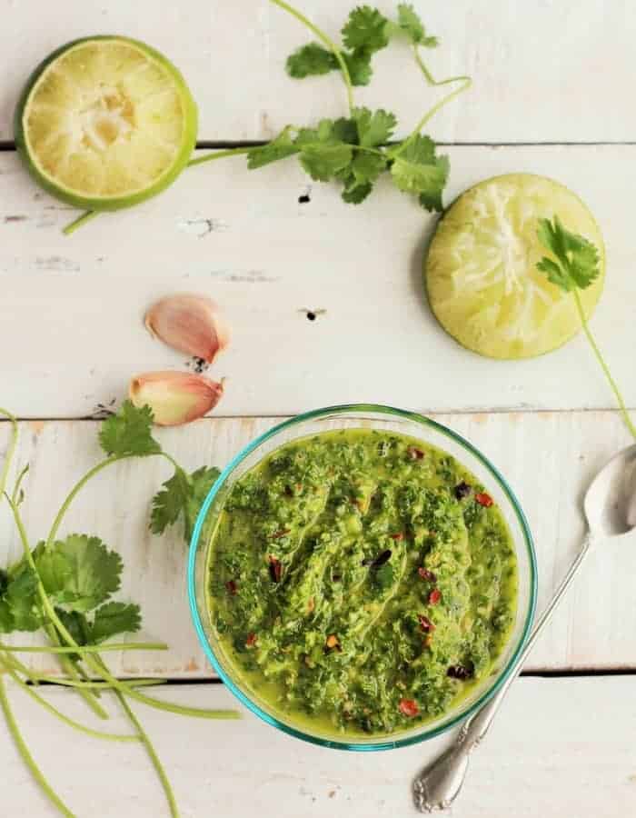 homemade chimichurri in a bowl with limes, cilantro and garlic on a white board