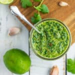 a glass jar with cilantro chimichurri and herbs on a white board