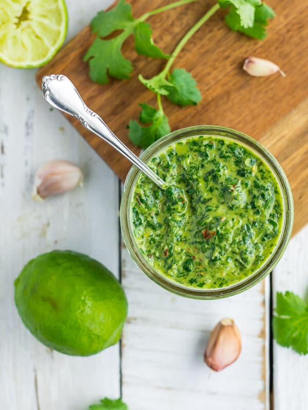 a glass jar with cilantro chimichurri and herbs on a white board