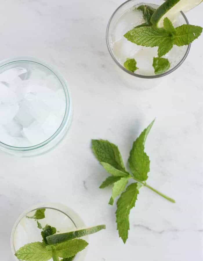 Virgin mojitos, mint, and a bowl of ice on a white background