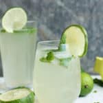 Two glasses of virgin mojitos with lime and mint on a white board