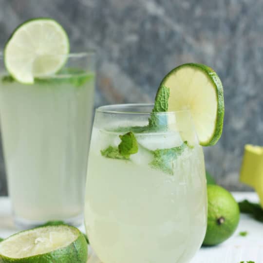 Two glasses of virgin mojitos with lime and mint on a white board
