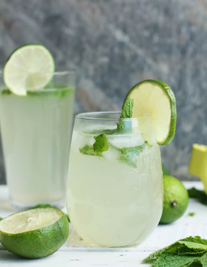 Two glasses of a virgin mojito with lime and mint on a white board