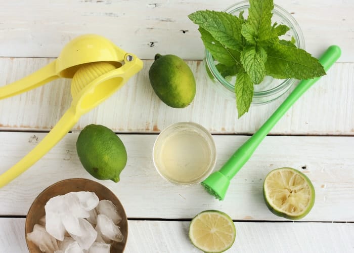 lime, mint, and ice on a white board with a citrus squeezer for making a mojito mocktail