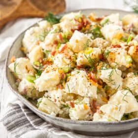 A bowl of instant pot potato salad topped with dill, bacon, and green onions