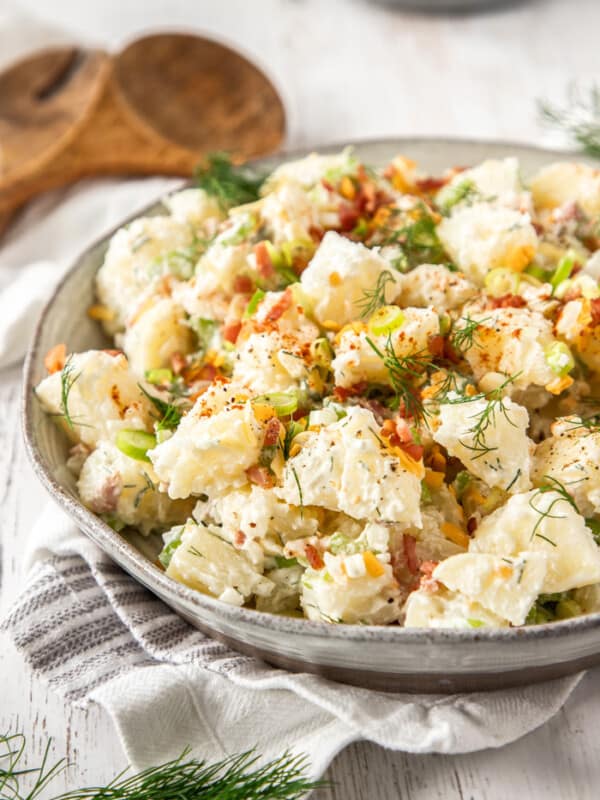 A bowl of instant pot potato salad topped with dill, bacon, and green onions