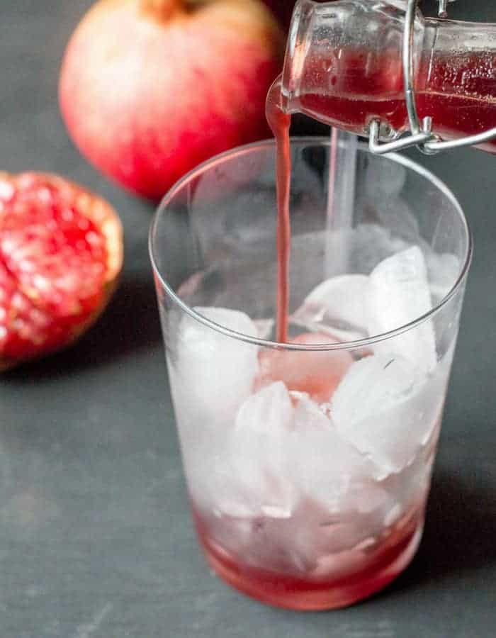 homemade grenadine being poured into a glass of ice