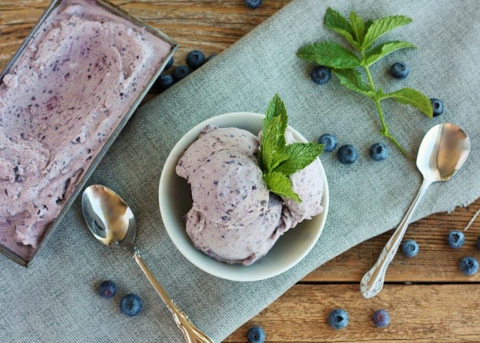 A bowl of blueberry ice cream with mint on a grey cloth