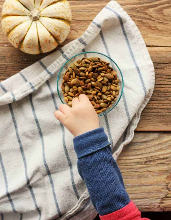 a toddler's hand reaching for white cheddar pumpkin seeds on a white cloth