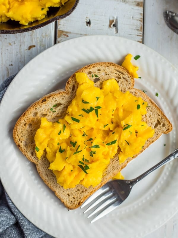 A white plate with toast and scrambled eggs topped with chopped parsley