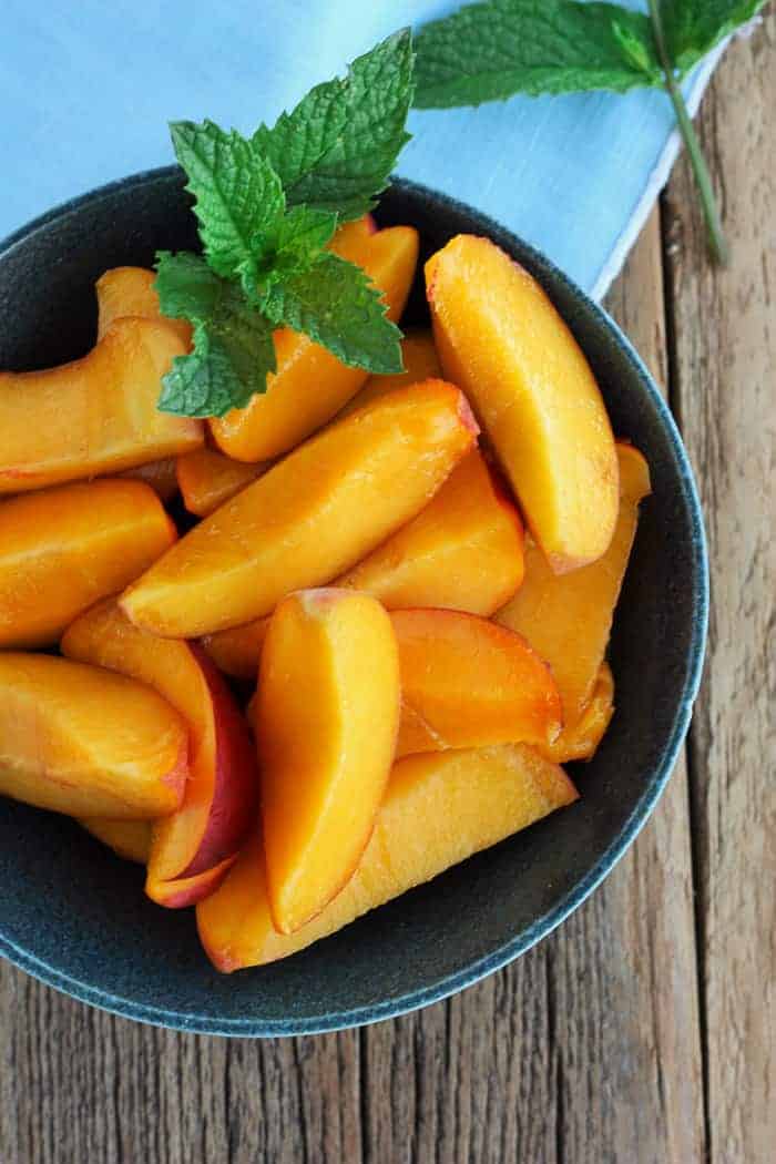 a bowl of sliced peaches with mint