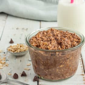 a glass jar with chocolate overnight oats on a white board with a small bottle of milk