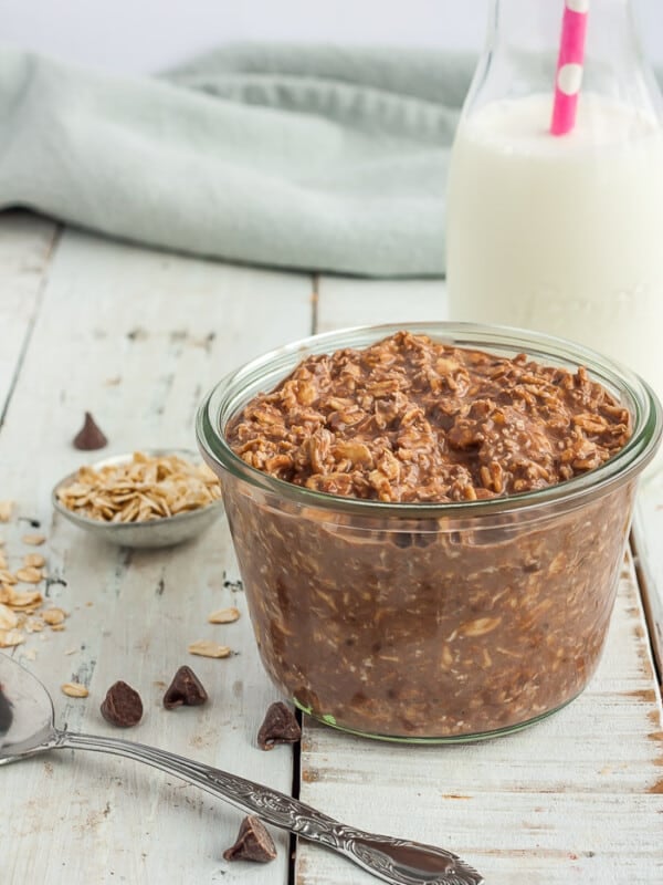 a glass jar with chocolate overnight oats on a white board with a small bottle of milk