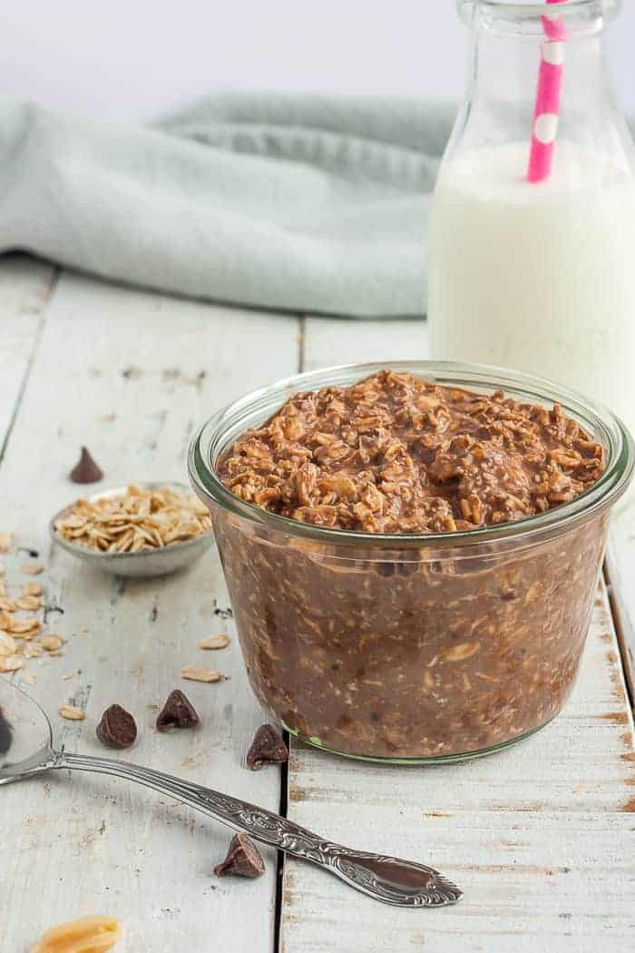 a glass jar with chocolate overnight oats on a white board with a small bottle of milk