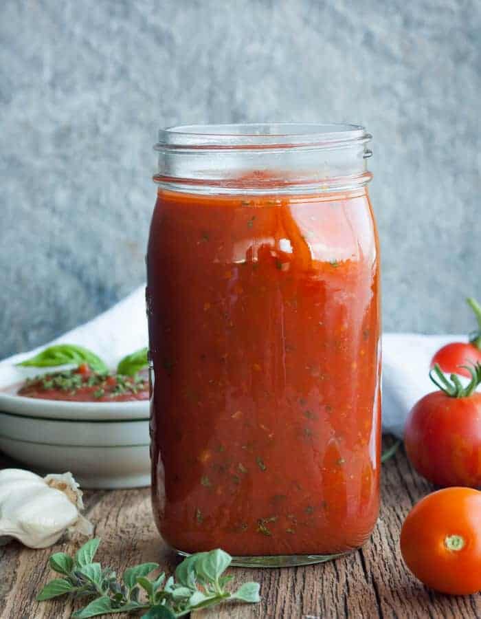 a jar of spaghetti sauce with herbs and fresh tomatoes.
