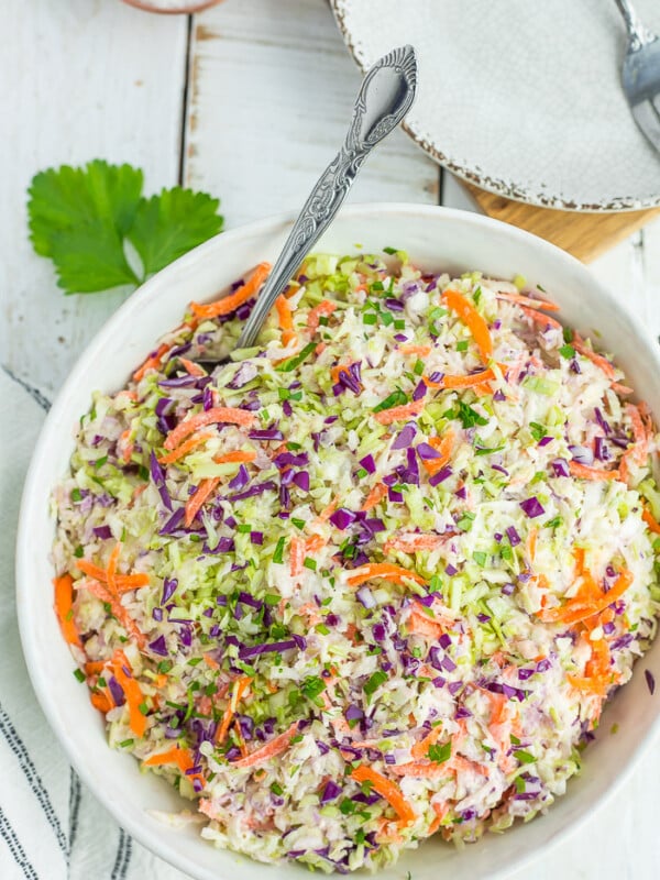 a multi-colored coleslaw in a white bowl with a spoon on a white board