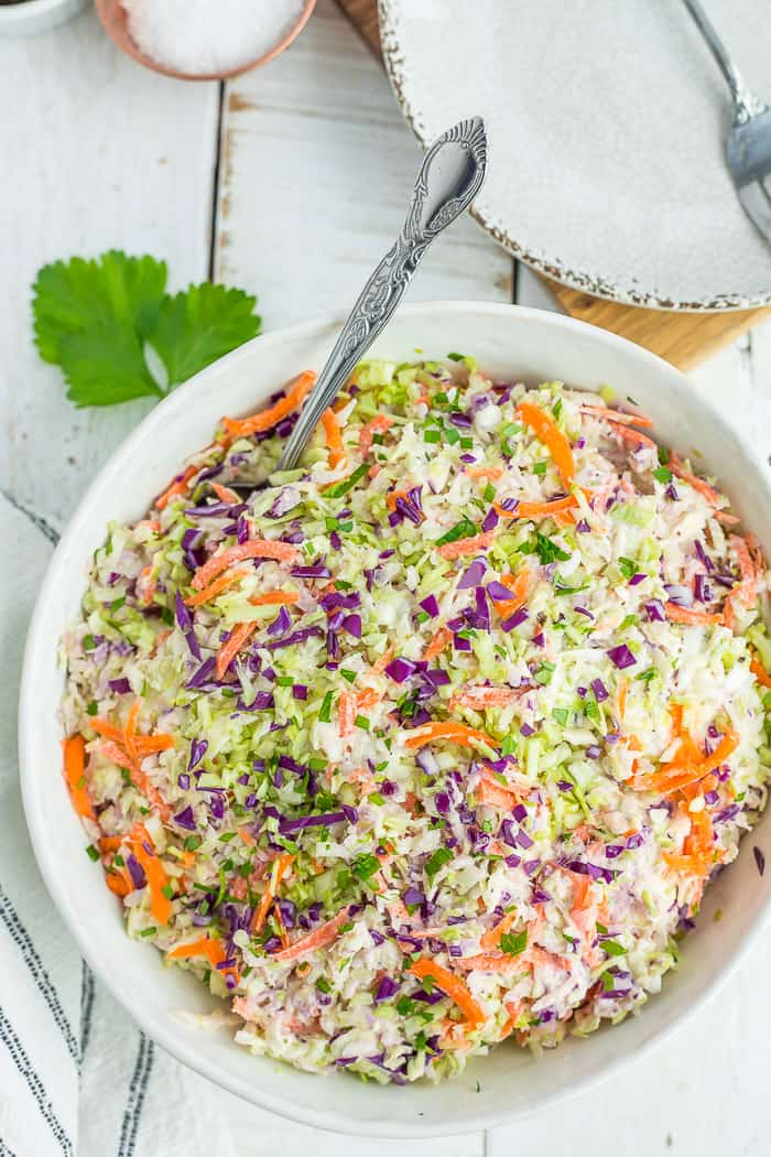 a multi-colored coleslaw in a white bowl with a spoon on a white board