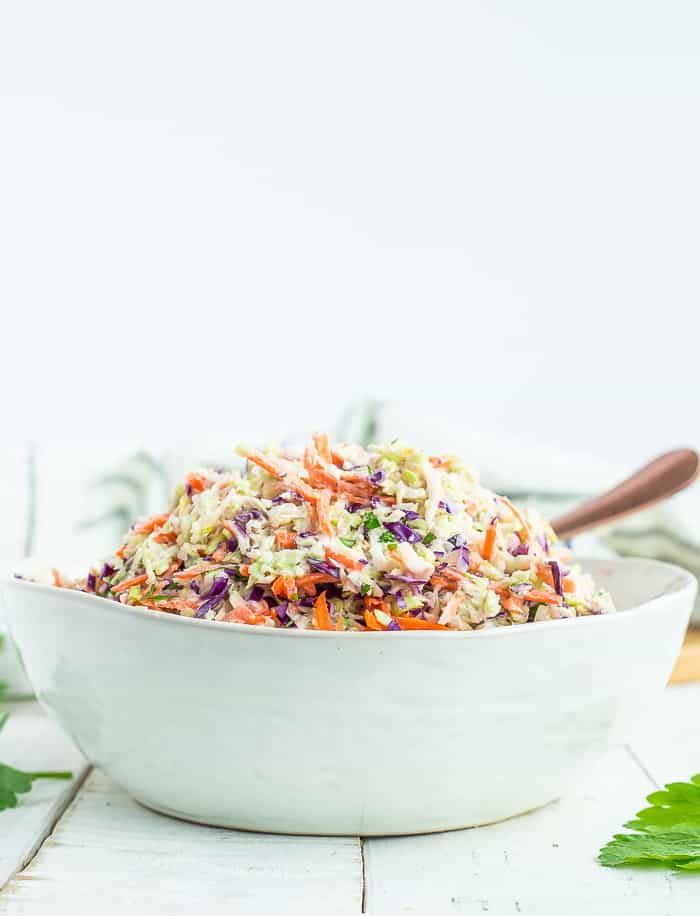 a white bowl full of healthy coleslaw with a spoon 