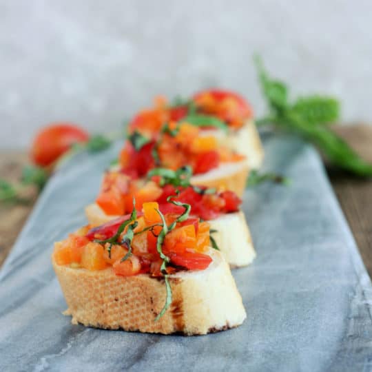 four pieces of tomato bruschetta on a grey cheese board
