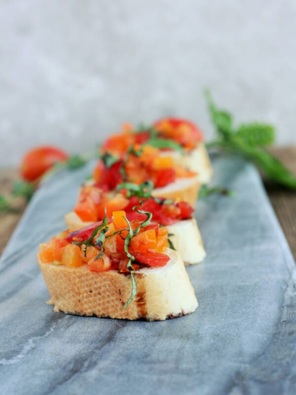 four pieces of tomato bruschetta on a grey cheese board