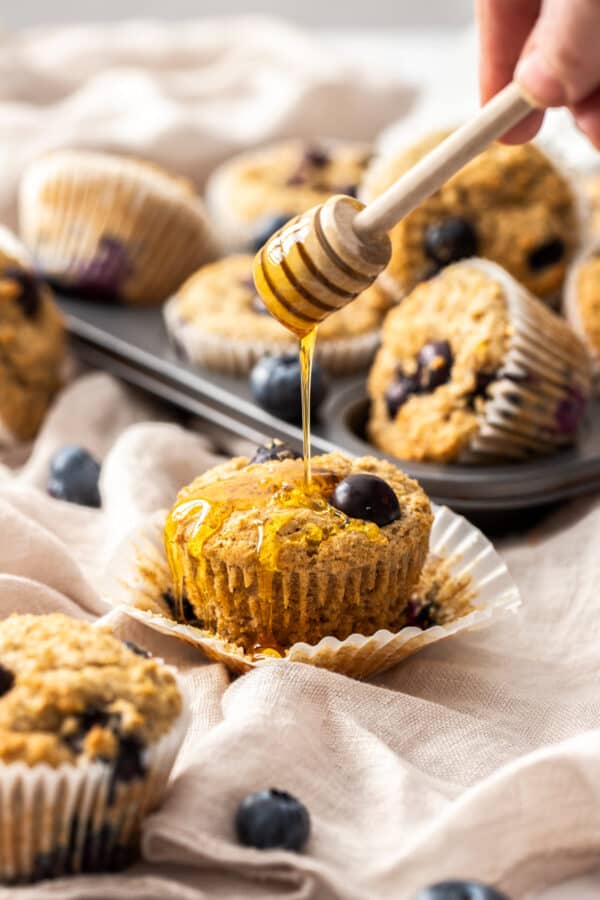 honey being drizzled over a whole wheat blueberry muffin