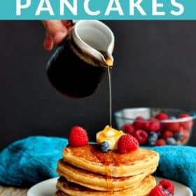 A stack of whole wheat pancakes topped with berries and butter and syrup being poured over it
