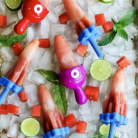 A tray of homemade watermlon popsicles on ice with mint and lime