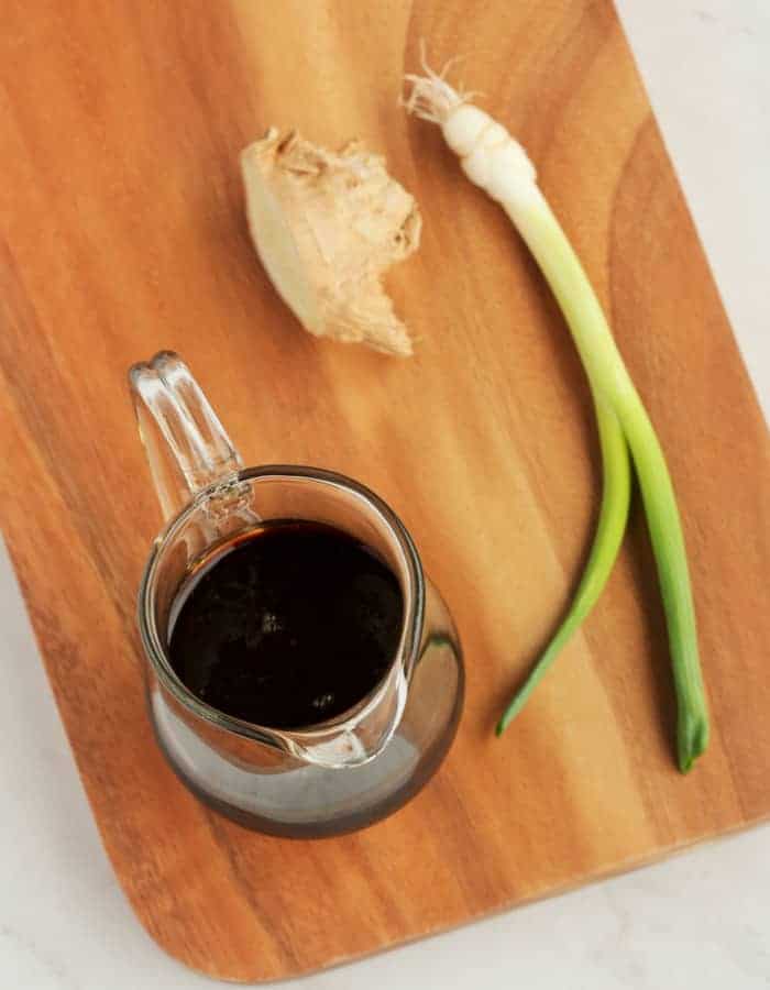 gluten free teriyaki sauce on a cutting board with ginger and a scallion