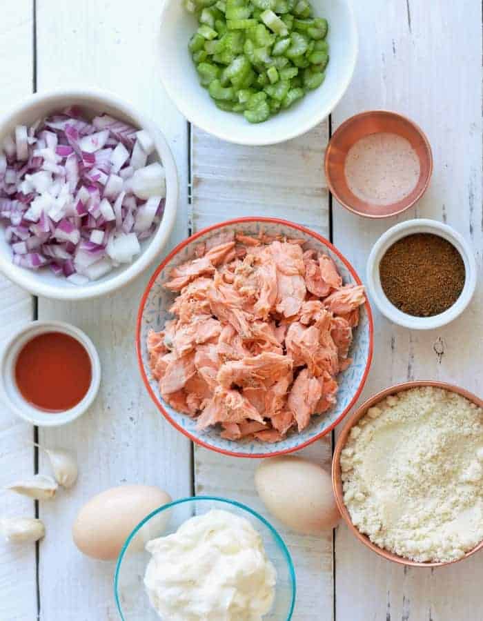 Salmon, onion, eggs, and other ingredients for paleo salmon cakes on a white board