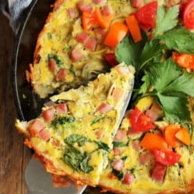 A slice of quiche with hash brown crust in a cast iron pan