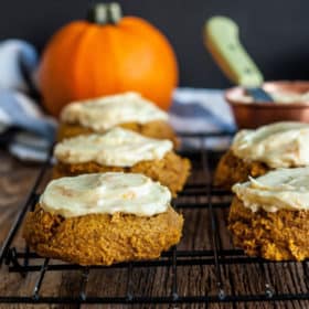 whole wheat soft pumpkin cookies with frosting on a cooling rack with pumpkins in the background