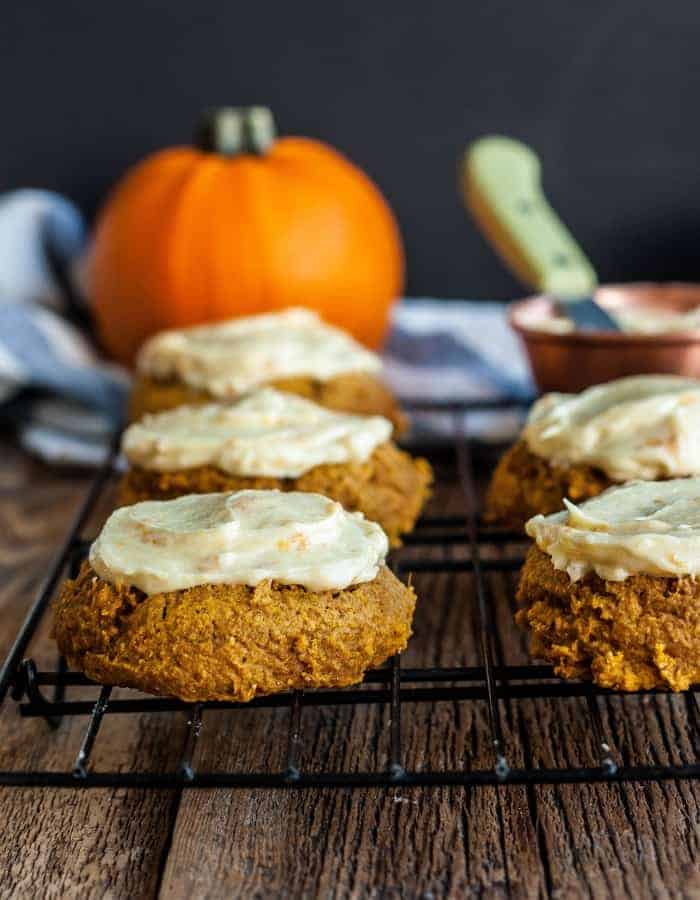 whole wheat soft pumpkin cookies with frosting on a cooling rack with pumpkins in the background