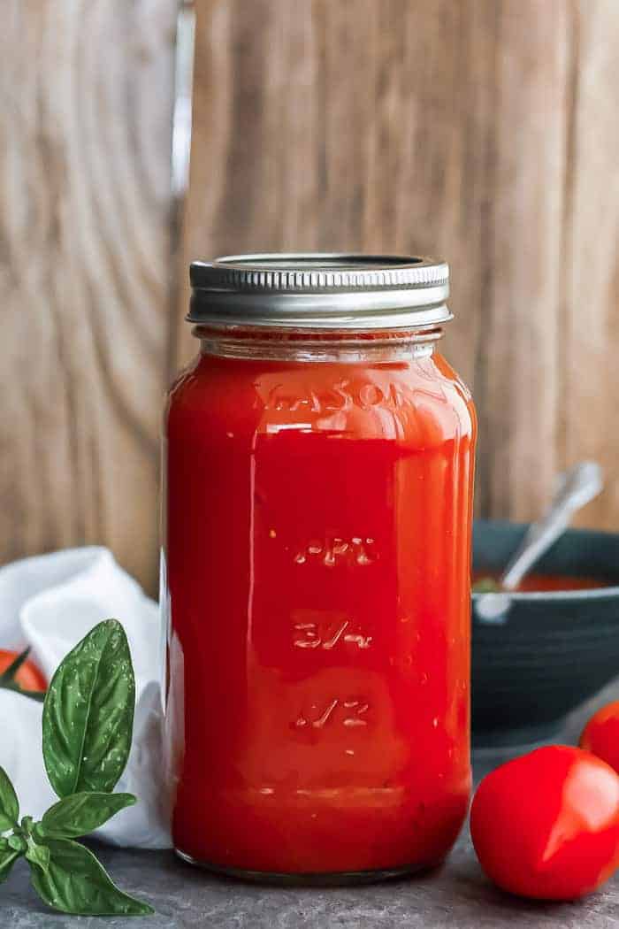 a quart jar of tomato soup with basil on a wooden board