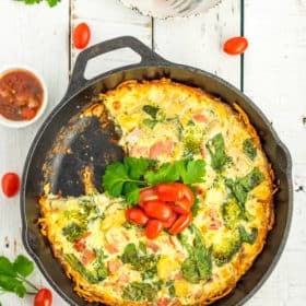 gluten-free quiche in a cast iron skillet topped with parsley and sliced tomatoes