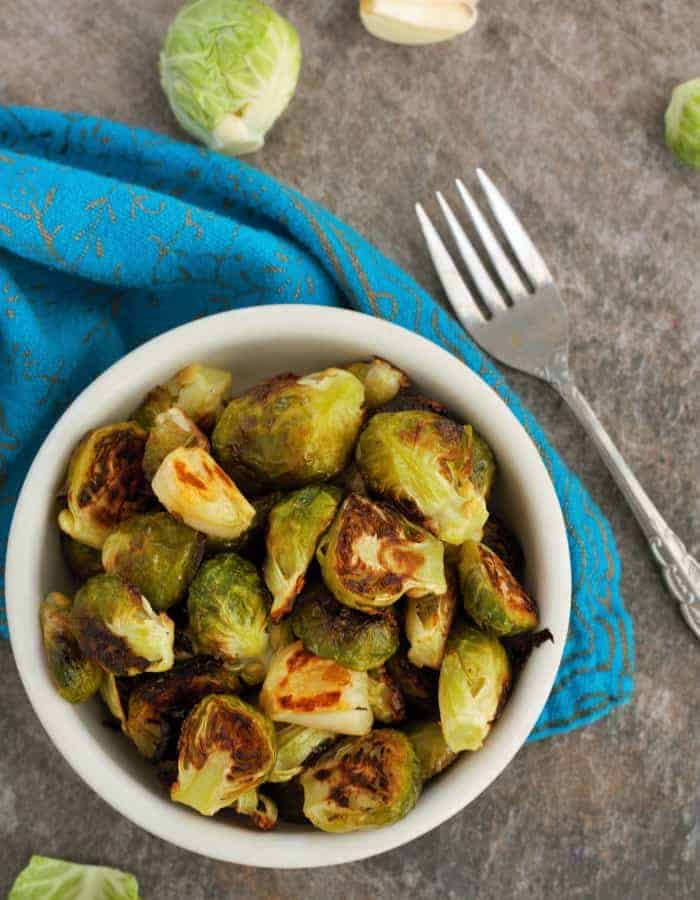 A bowl of roasted brussels sprouts with garlic, a fork, and blue cloth