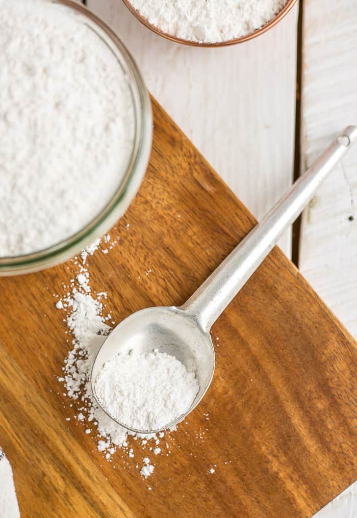 a spoon and glass of powdered sugar on a wooden cutting board