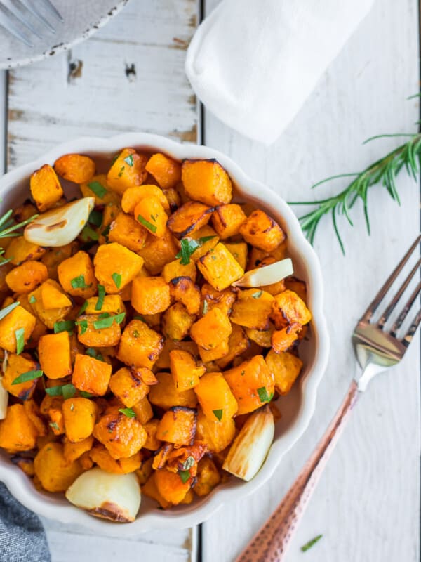 a white scalloped bowl with cubes of crispy butternut squash with afork on a white board