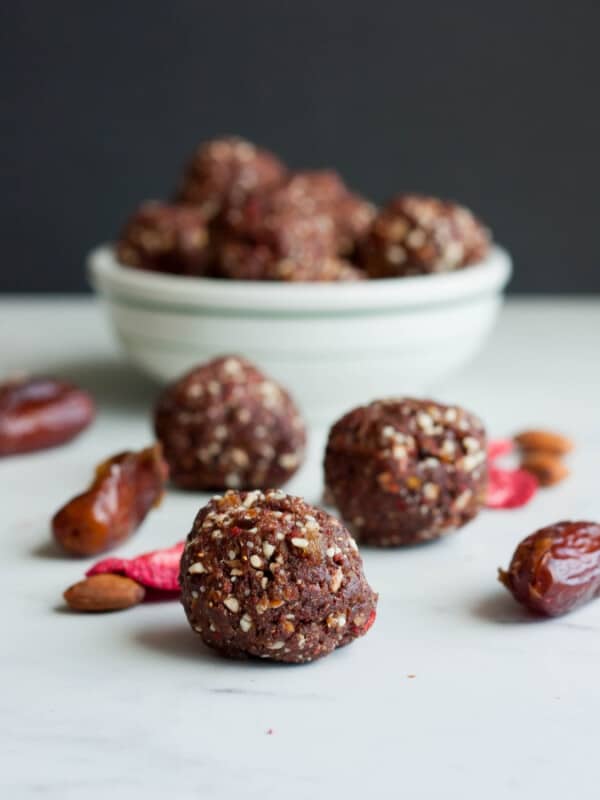 strawberry fudge energy date balls in a bowl with 3 on a white board with dates and dried strawberries