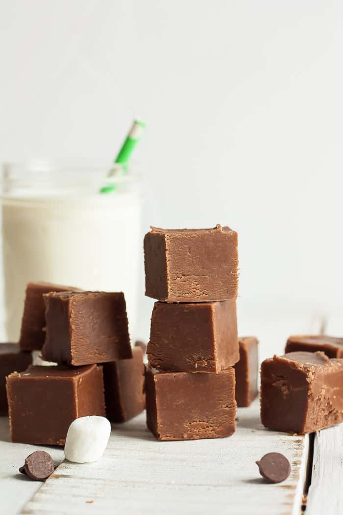 squares of fudge stacked on a white board with a canning jar of milk