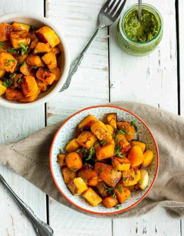 Two bowls of oven-roasted butternut squash with chimichurri sauce on a white board