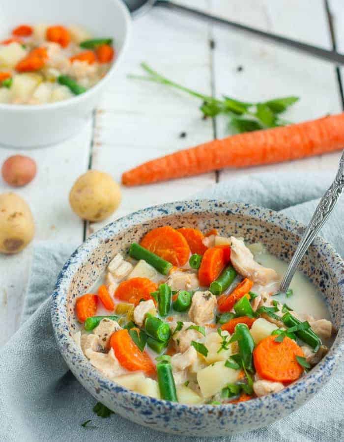 a bowl of paleo chicken pot pie soup with carrots and potatoes in the background