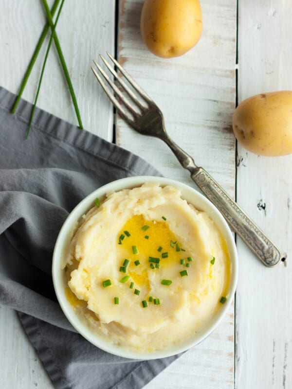 a bowl of whole30 mashed potatoes with a fork, chives, and mini potatoes on a white board