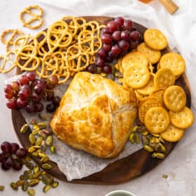 puff pastry wrapped baked brie on a cheese board with pretzels, crackers, and grapes