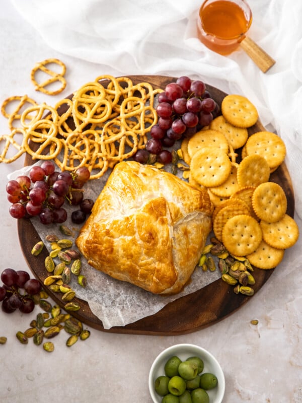 puff pastry wrapped baked brie on a cheese board with pretzels, crackers, and grapes