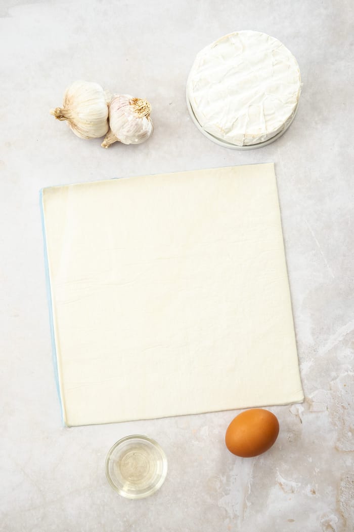 puff pastry, brie, an egg, and garlic on a white board