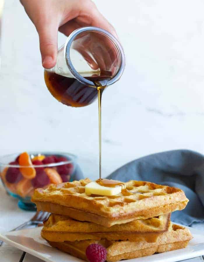 Maple syrup being poured over a stack of eggnog waffles