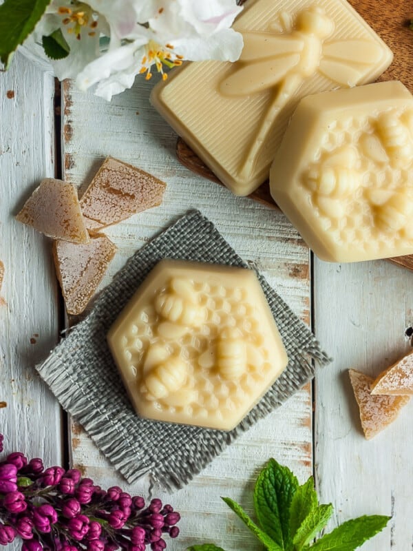 a lotion bar in the shape of honeycomb on a grey cloth with wax and other lotion bars on a white board